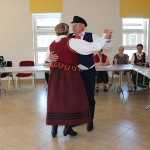 Kobieta i mężczyzna tańczy w parze , reszta uczestników spotkania przygląda się.