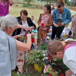 Grupa osób dorosłych i dzieci wije wianki z kwiatów