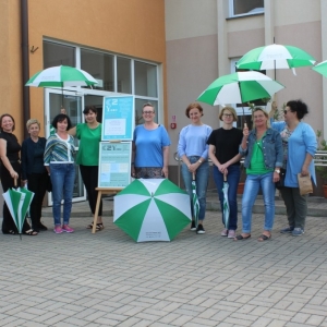 Grupa kobiet pozyje do zdjęcia przed budynkiem z parasolami.