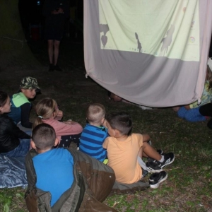 9Przy dużym ekranie siedzą dzieci, z jednej strony osoby biorące udział w przedstawieniu, a z drugiej widzowie.