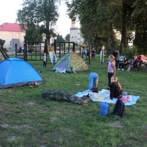 Na placu rozstawione namioty,na kocu trzy dziewczynki, na placu zabaw bawią się dzieci.