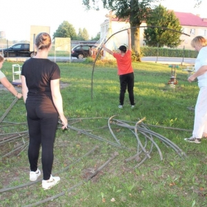 Cztery osoby rozkładają namiot,jedna osoba trzyma długą rurkę,reszta spogl ąda na ziemię.