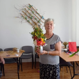 Kobieta stoi i uśmiecha się trzymając w ręku bukiet.