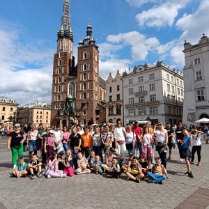 Grupa kobiet, mężczyzn i dzieci pozuje do zdjęcia. W tle kościół Mariacki w Krakowie.