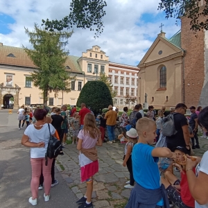 Grupa kobiet, mężczyzn i dzieci na ulicy przy kościele przed oknem papieskim.