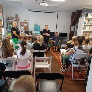 Bibliotekarka stoi przed publicznością, zapowiada temat spotkania i przedstawia prelegentkę.