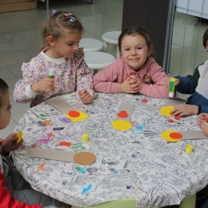 Gupka dzieci siedzą przy małym stoliku i sklejają zakładkę.