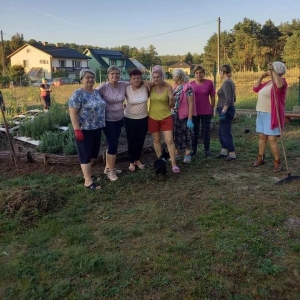 Grupka kobiet stoją przed ogródkiem ziołowym.