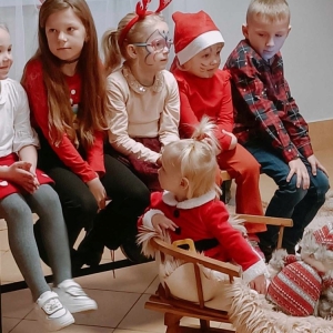 Cztery dziewczynki i chłopiec w świątecznych przebraniach siedzą na ławeczce, jedna mała dziewczynka siedzi na saneczkach