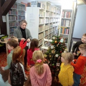 Grupa dzieci i bibliotekarka wieszają świąteczne ozdoby na choince