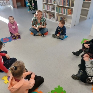 Uczestnicy ferii w bibliotece siedzą w kole, bibliotekarka przebrana za Pipi Pończoszankę czyta im książkę o Pipi