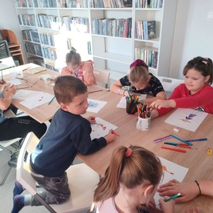 Uczestnicy ferii w bibliotece siedzą przy stole, rysują portret Pipi Pończoszanki