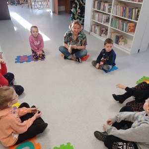 Uczestnicy ferii w bibliotece siedzą w kole, bibliotekarka przebrana za Pipi Pończoszankę czyta im książkę o przygodach Pipi