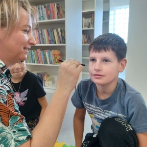 Bibliotekarka maluje chłopcu piegi na twarzy