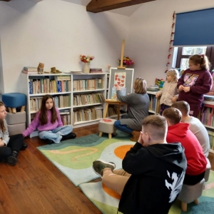 Uczestnicy ferii w bibliotece wraz  z bibliotekarką rozmawiają o Święcie Babci i Dziadka