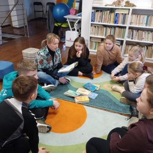 Bibliotekarka i dzieci siedzą na dywanie, kobieta czyta im książkę