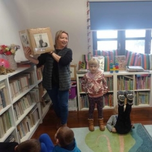 Bibliotekarka pokazuje dzieciom obrazek z zadanym ćwiczeniem gimnastycznym