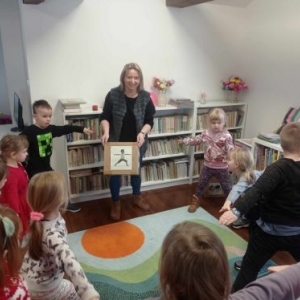 Bibliotekarka pokazuje dzieciom obrazek z zadanym ćwiczeniem gimnastycznym