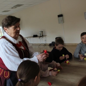 Prowadząca warsztaty pokazuje jak robić kwiaty z bibibuły.