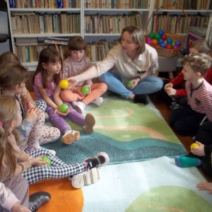 Bibliotekarka z dziećmi w trakcie wiosennej wyliczanki podają sobie piłeczkę