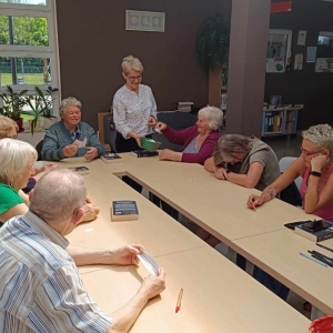 Przy stole siedzą seniorzy prowadząca rozdaje im karteczki.