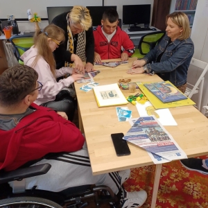 Opiekunka grupy i bibliotekarka pomagają uczestnikom robić papierowe czapki