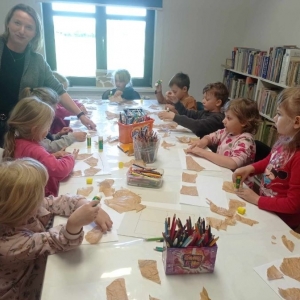 Bibliotekarka objaśnia dzieciom jak wykonać pracę plastyczną