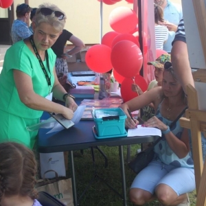 Kobieta w zielonej sukience obsługuje stoisko biblioteki