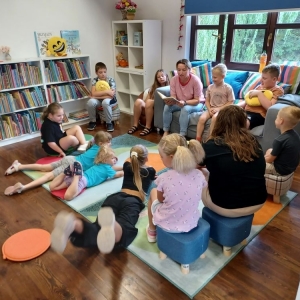 Uczestnicy wakacyjnych warsztatów słuchają ballady czytanej przez bibliotekarkę 