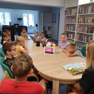 Uczestnicy spotkania w bibliotece słuchają wiersza, który czyta im koleżanka