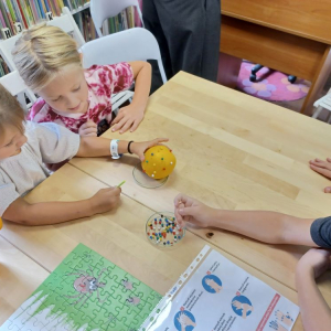  Dwie dziewczynki ćwiczą technikę wyjmowania kleszcza podczas spotkania edukacyjnego w bibliotece