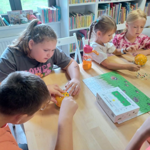 Dzieci ćwiczą technikę wyjmowania kleszcza podczas spotkania edukacyjnego w bibliotece