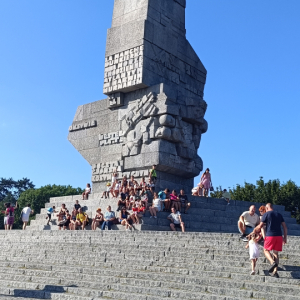 Uczestnicy wyjazdu siedzą pod pomnikiem na Westerplatte