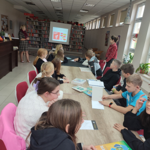 Młodzież na spotkaniu edukacyjnym w bibliotece słucha i śledzi prezentacje omawianą przez prowadzącą