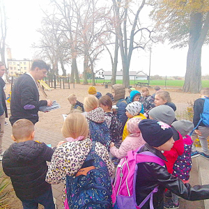 Pan Krystian Truchalski przed budynkiem biblioteki rozdaje książeczki dzieciom