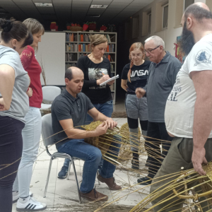 Instruktor pokazuje grupie uczestników jak wyplatać koszyk.