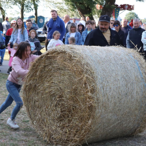 Dziewczynka toczy dużą belę słomy, w tle widzowie.