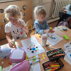 Dwie dziewczynki siedzące przy stoliku wykleja rysunek balona kolorowymi kropkami