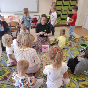 Bibliotekarka rozdaje dzieciom symbole święta - kolorowe kropki do przyklejenia na ubraniu