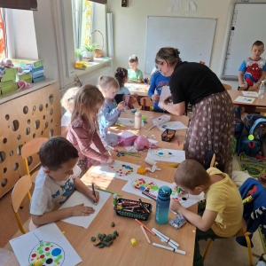 Bibliotekarka pomaga dzieciom wykonać prace plastyczne