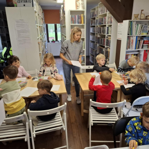 Opiekunka rozdaje dzieciom kartki do rysunków.