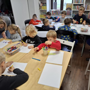 Grupa dzieci zajęta rysowaniem, pani opiekunka pomaga małej dziewczynce