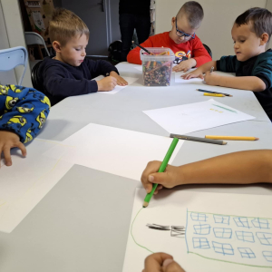 Kilku chłopców przy stoliku rysuje na kartkach.