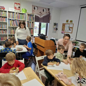 Grupa dzieci rysuje, dwie panie czuwają nad ich pracą.