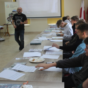 Młodzież siedząca przy stole sięga po kartki