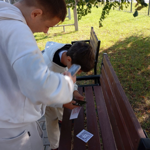 Dwóch chłopców skanuje kod QR leżący na ławce.