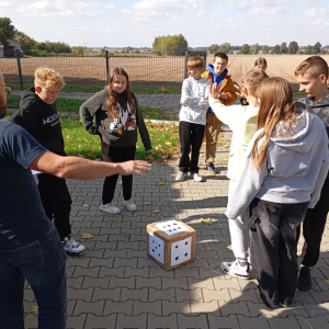 Grupa młodzieży testuje z prowadzącym grę planszową na parkingu przed biblioteką