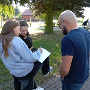 Prowadzący i dwie dziewczyny rozmawiają na placu przed biblioteką.
