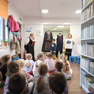 Przed grupą siedzących dzieci dwie panie z KGW opowiadają o dawnych strojach ludowych.