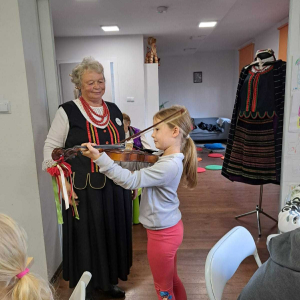 Grająca na skrzypcach dziewczynka stoi obok kobiety ubranej w strój ludowy.